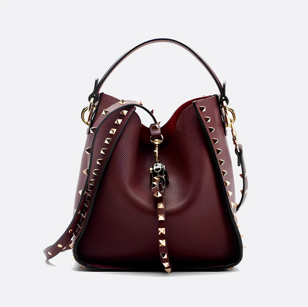 A burgundy pebbled leather bucket bag with gold-tone studs and a matching top handle, shown on a light gray background.