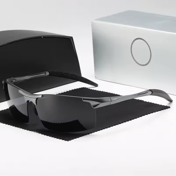 Black sunglasses with silver frame on a black cloth, next to a white box with a logo.