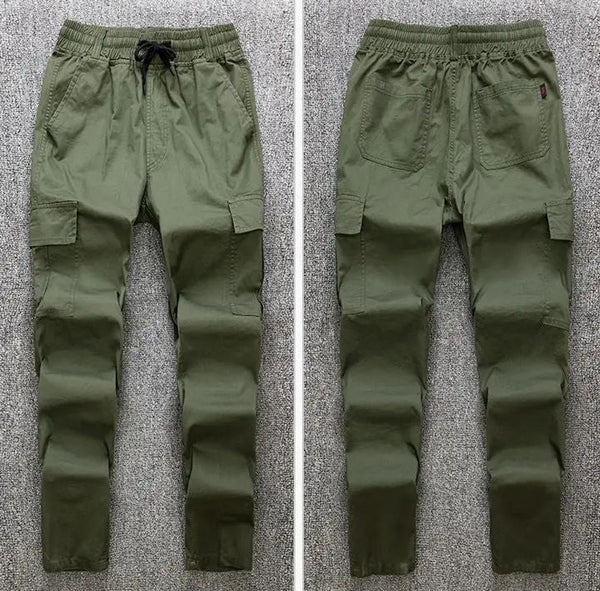 A pair of men's cargo pants shown from both the front and back views, laid flat on a gray textured carpet. The pants are olive green with an elastic waistband, black drawstring, and side cargo pockets.